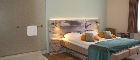 A modern bedroom with a large bed, a nightstand, a chair, and a shower area.