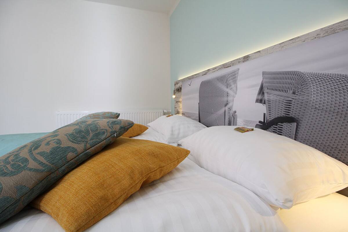 A neatly made bed with white and mustard pillows, a patterned pillow, and a headboard with a cityscape design.