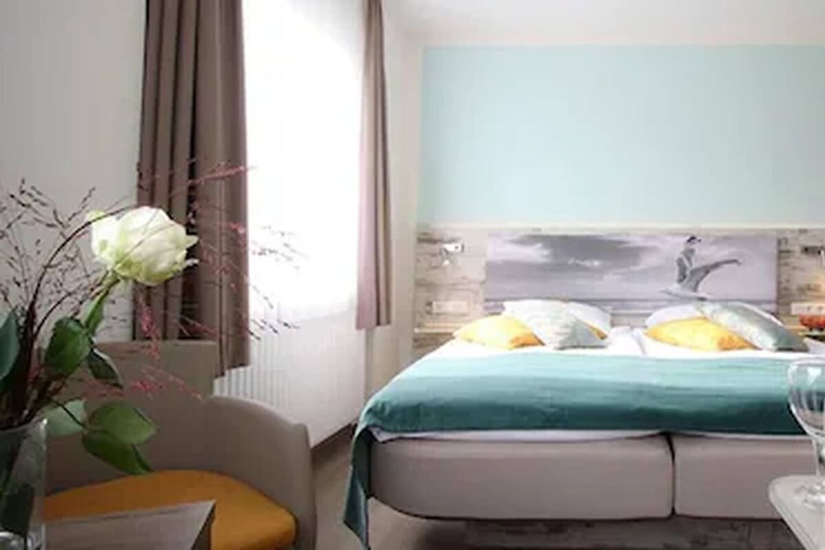 A hotel room with a bed, a nightstand, a vase with flowers, and a bottle of water.