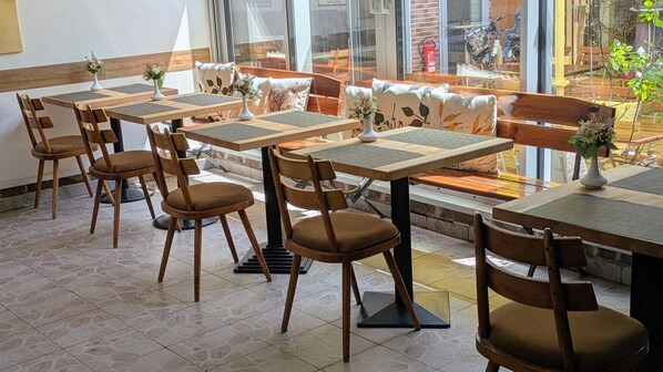 Un café con mesas y sillas de madera, un banco y vista a la calle.