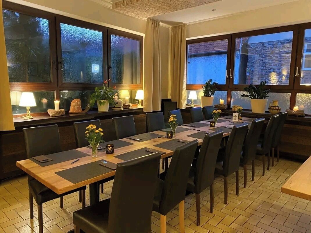 Un comedor con una mesa larga, sillas y plantas en macetas.