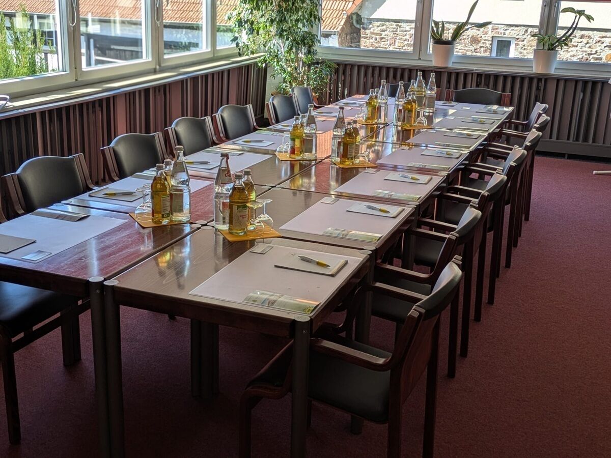 Un salón de conferencias con una mesa larga, sillas y botellas de agua.