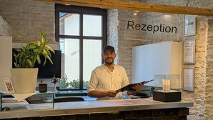 A reception desk with a person holding a tablet, a potted plant, and a sign that reads 'Rezeption' on the wall. - Hotel Sonne (Karlsruhe)