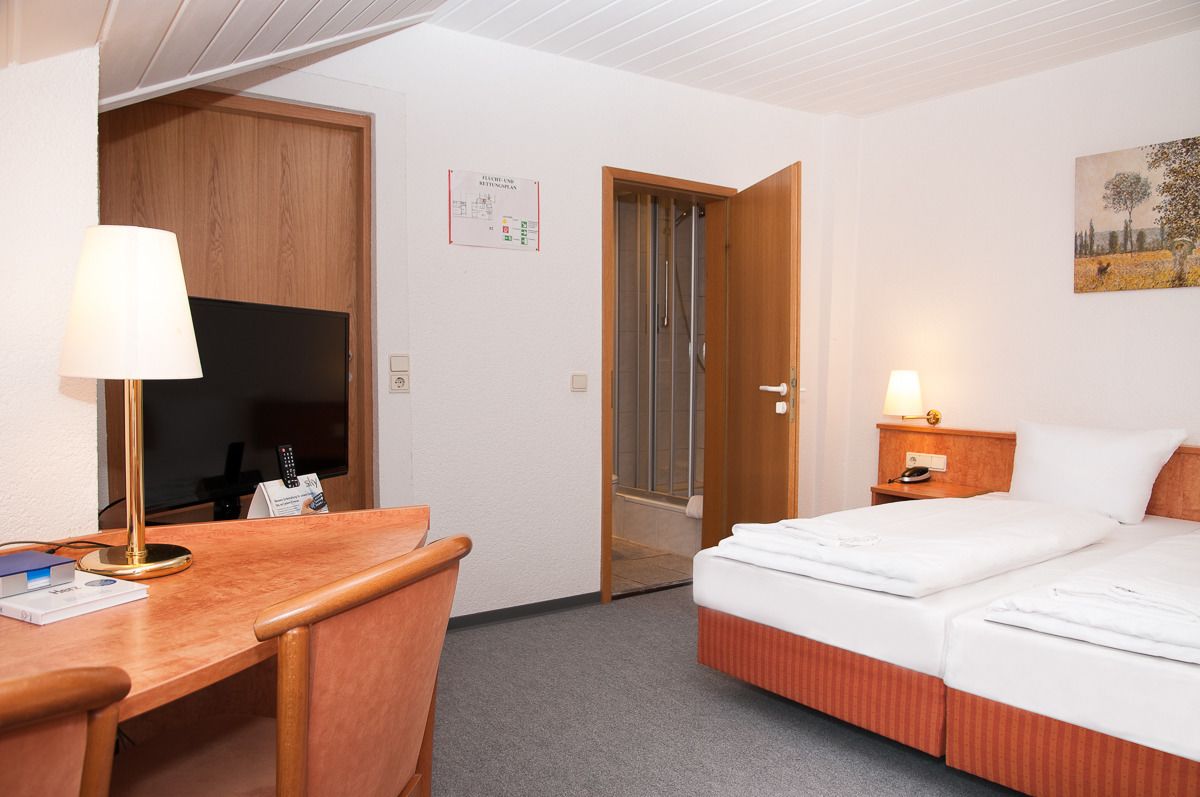 Una habitación de hotel con escritorio, cama, televisión y ducha.