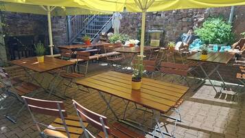 An outdoor patio with wooden tables and chairs, yellow umbrellas, and potted plants.
