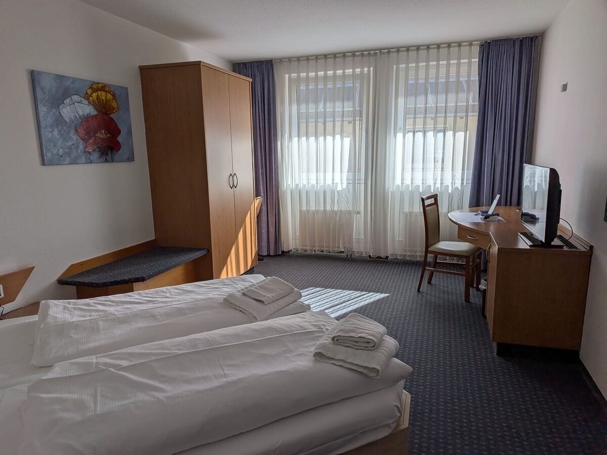 Ein Hotelzimmer mit zwei Betten, einem Schreibtisch, einem Stuhl, einem Kleiderschrank und einem Bild an der Wand.
