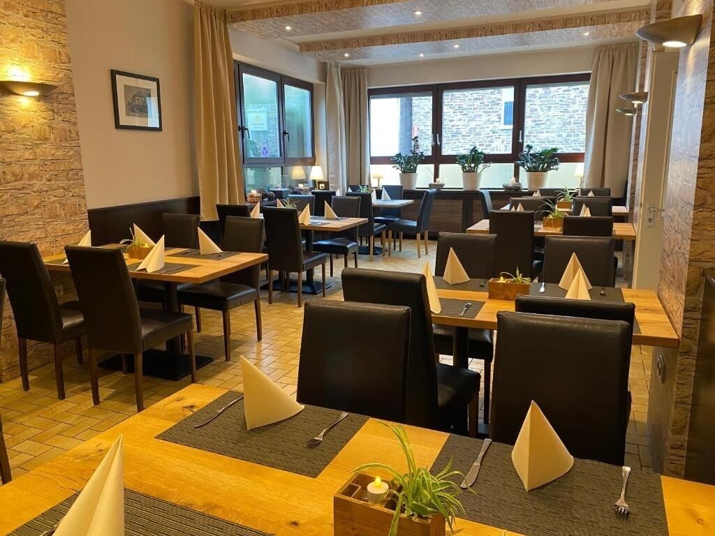 Un ristorante con diversi tavoli e sedie, ampie finestre e piante in vaso.