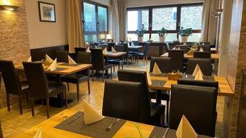 Un ristorante con diversi tavoli e sedie, ampie finestre e piante in vaso.
