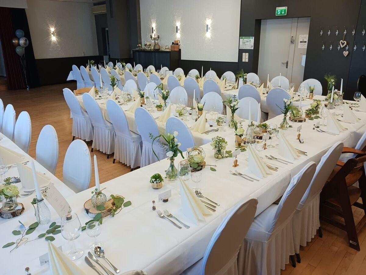 Un salón de banquetes con mesas largas, sillas blancas y centros de mesa florales.