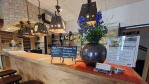 A hotel reception area with a wooden counter, bar stools, hanging pendant lights, a large vase with flowers, and a menu board. - Hotel Sonne (Karlsruhe)