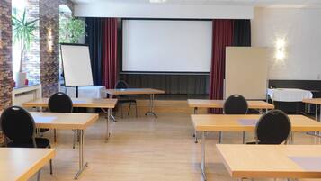 Un salón de conferencias con una pantalla grande, mesas de madera y sillas.