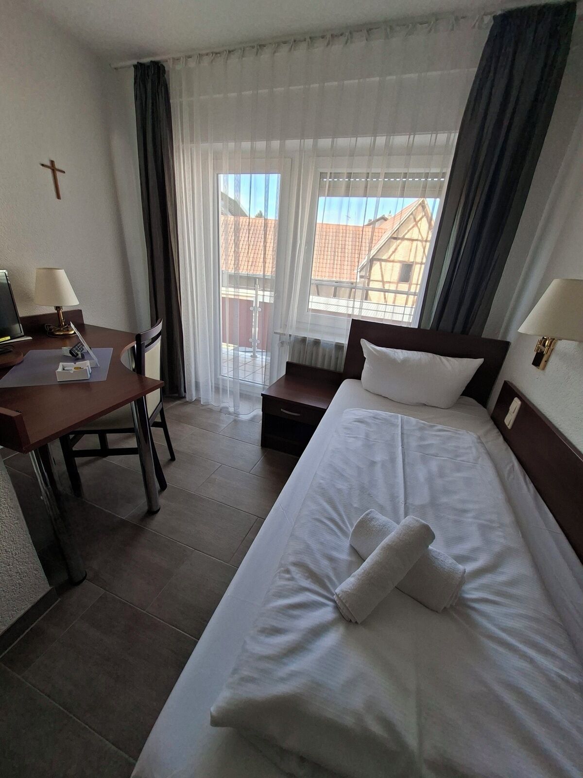 Habitación de hotel con cama, escritorio, silla, mesita de noche y ventana con cortinas.