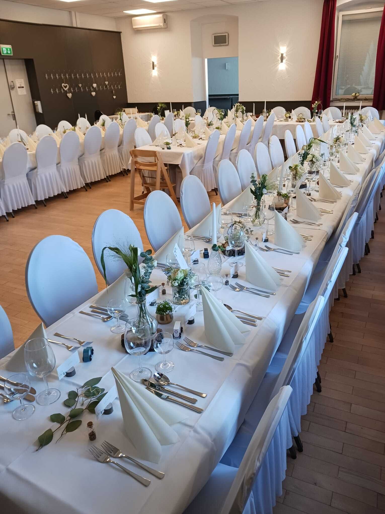 A banquet hall with long tables set for a formal event, white chairs, and a clean, organized layout.