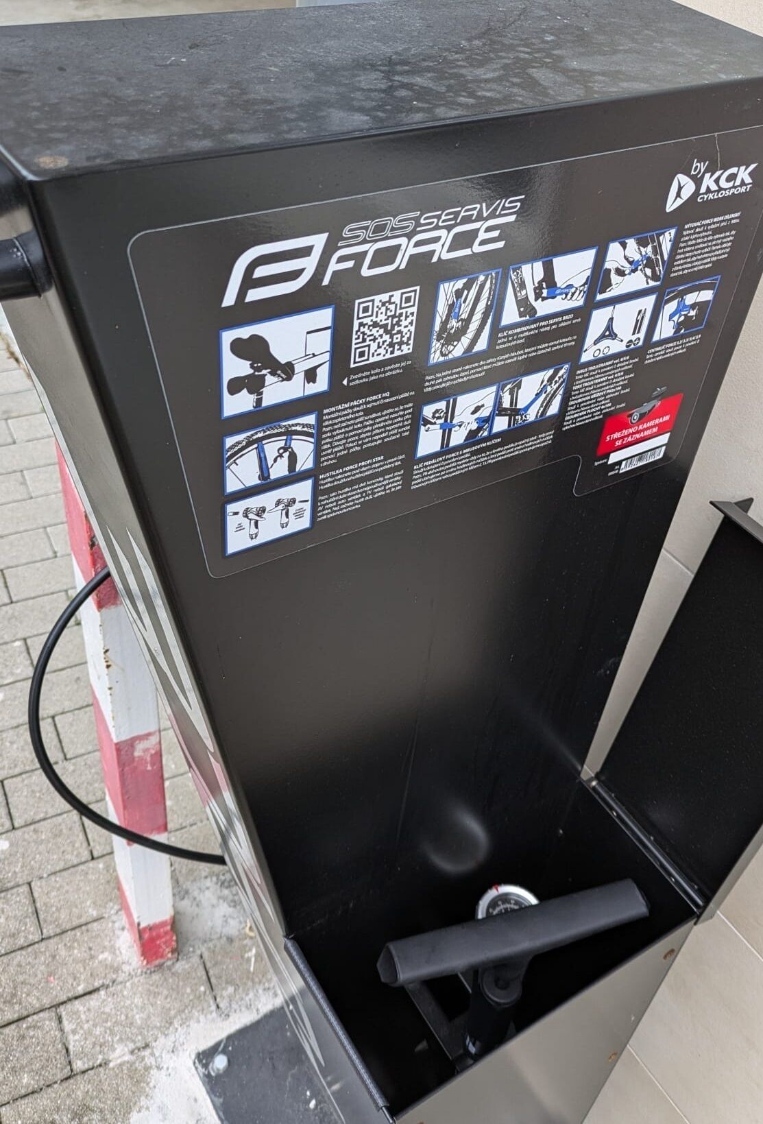 A black kiosk with a QR code, a logo, and instructional graphics.