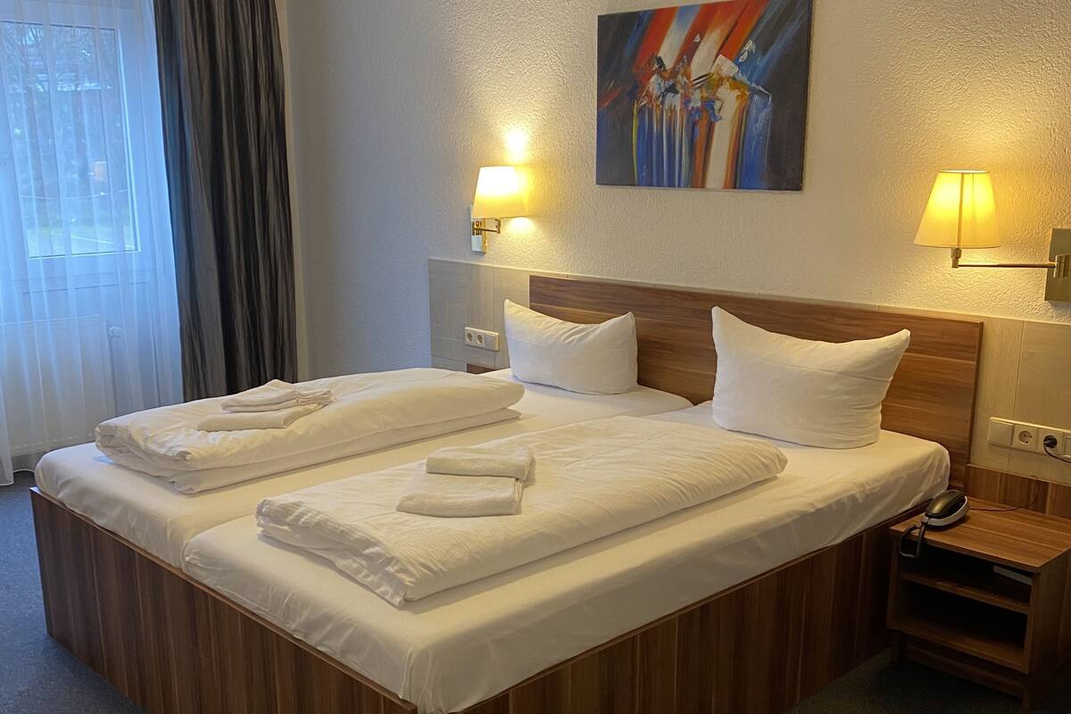 A hotel room with a large bed, two bedside lamps, a painting on the wall, and a nightstand with a phone and a lamp.