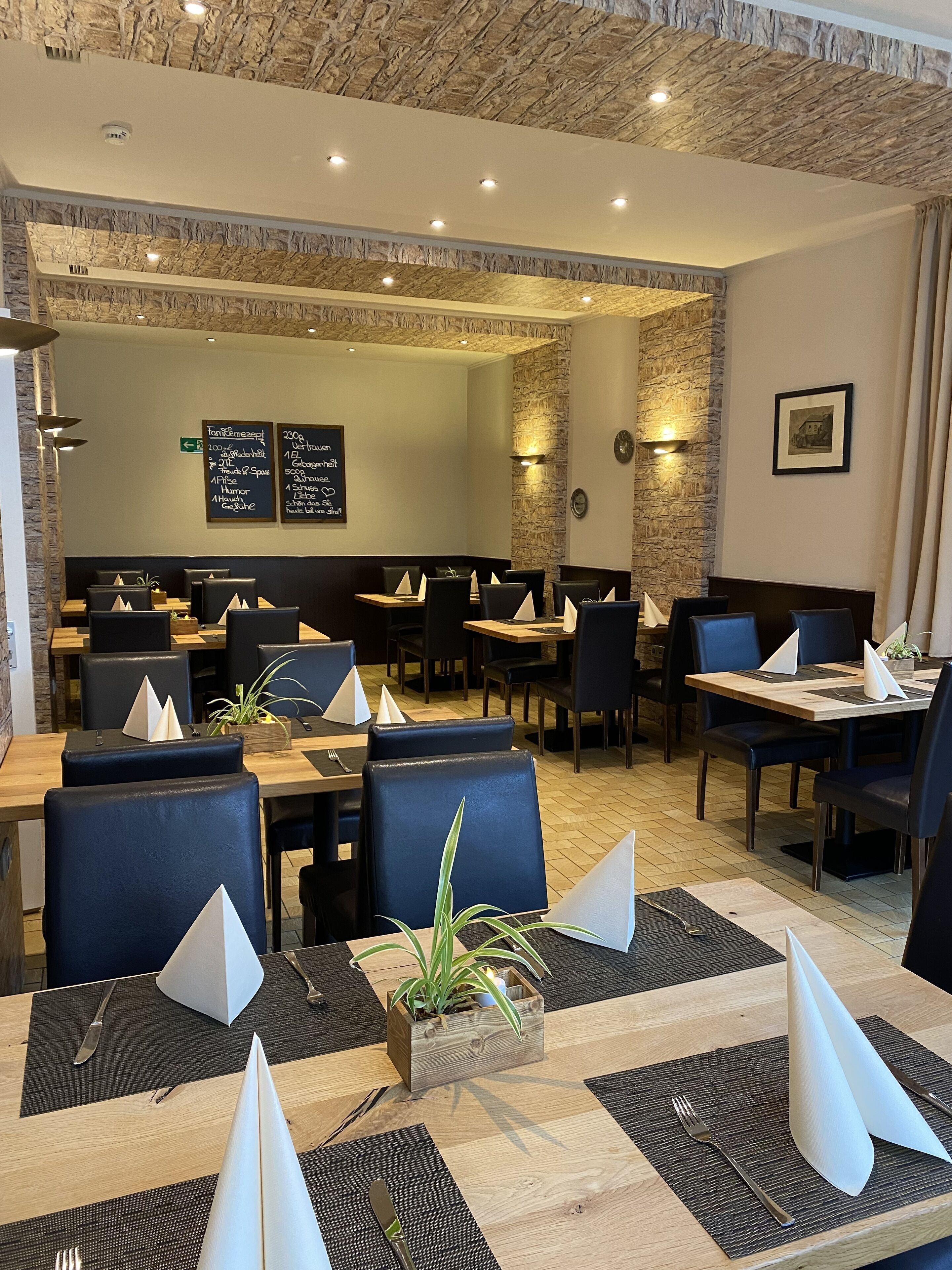 Interior de restaurante con varias mesas de comedor, sillas negras con acolchado y una pared de acento de piedra.