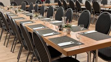 Sala de conferência com mesas longas, cadeiras pretas e louças postas.