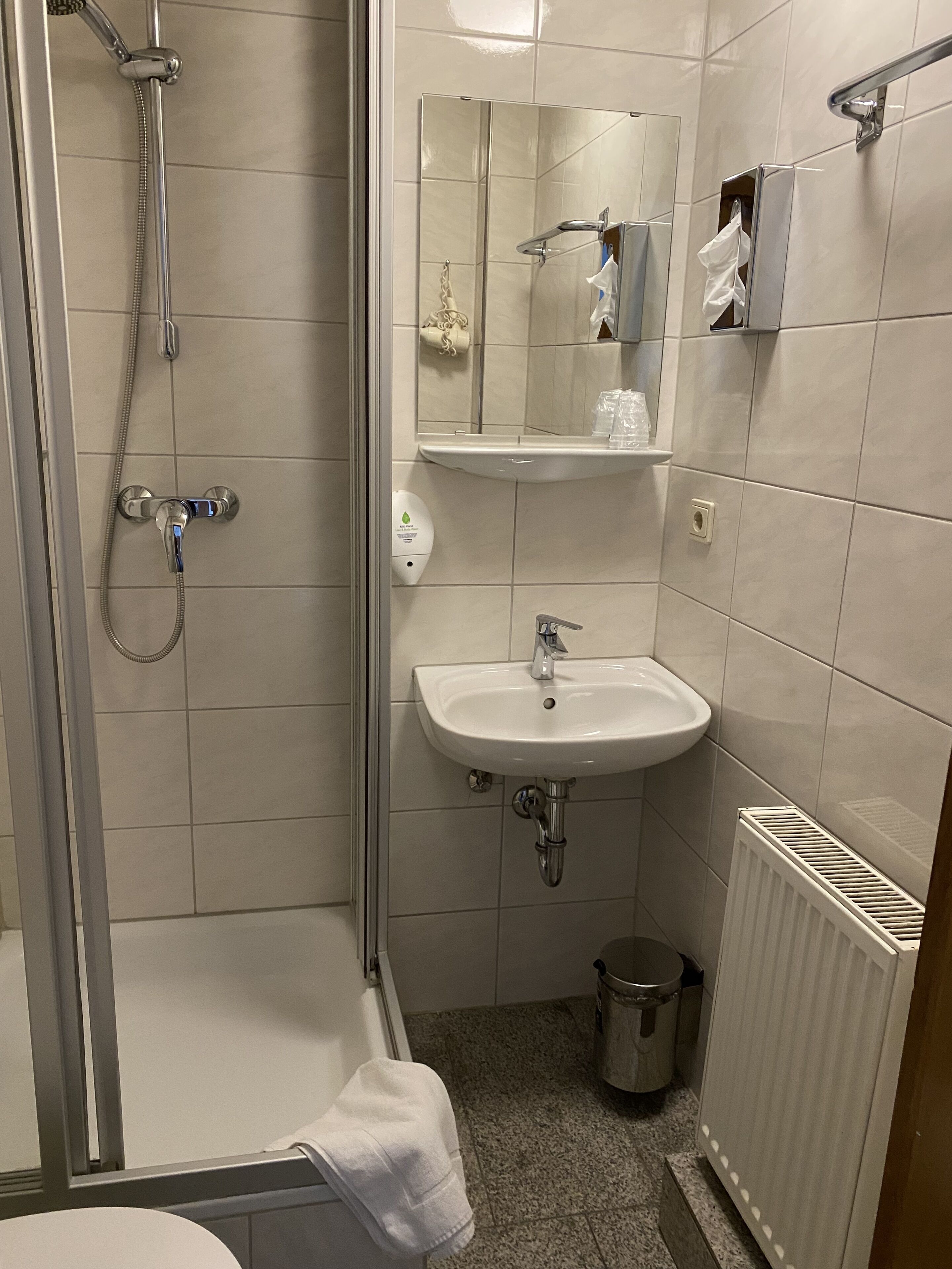 Ett modernt badrum med en duschkabin i glas, en vit tvättställ och en spegel ovanför.