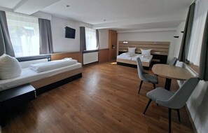 A hotel room with a wooden floor, two beds, a small round table, and a TV mounted on the wall. - Hotel Sonne (Karlsruhe)