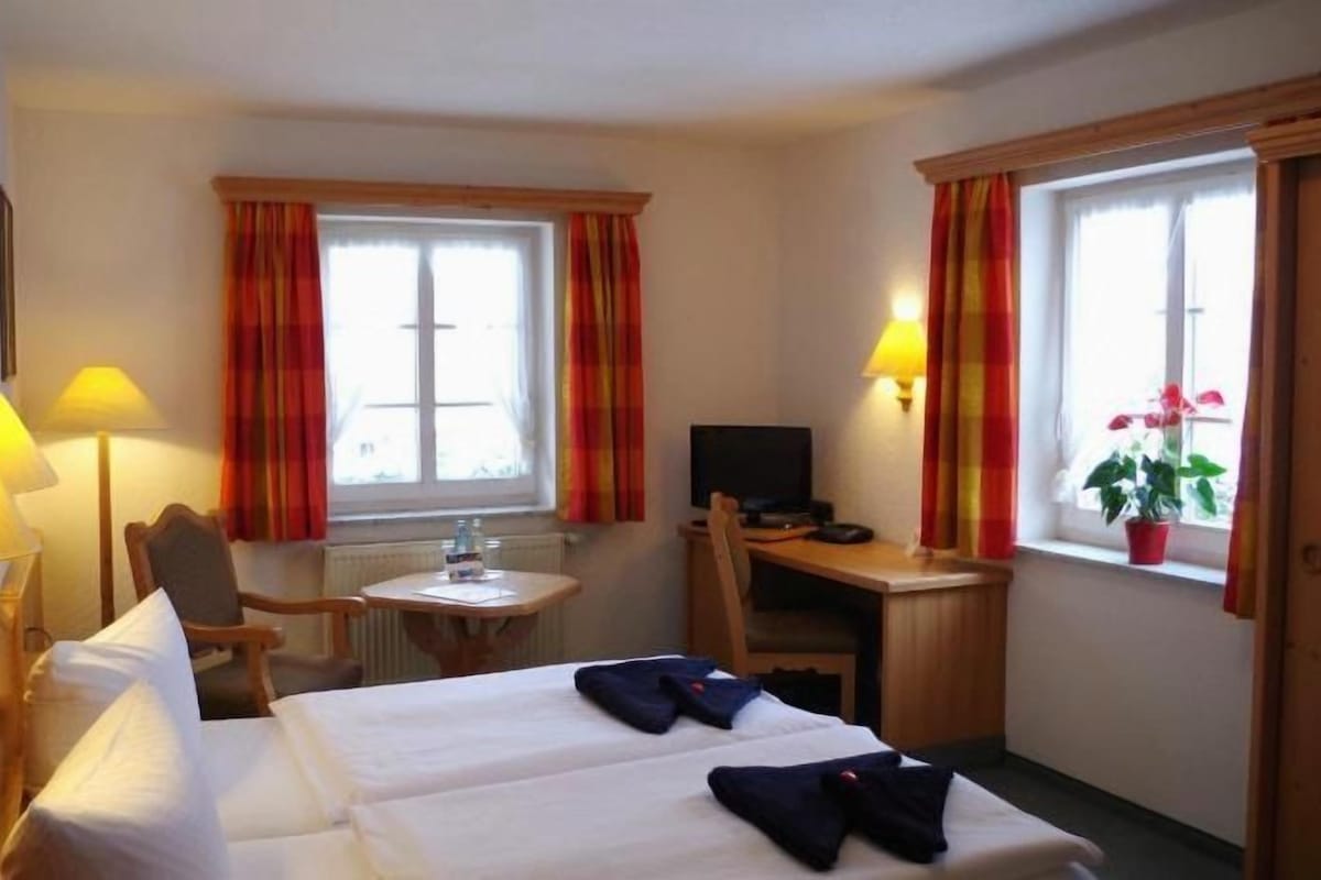 Habitación de hotel con dos camas, un escritorio, una silla, un televisor y una ventana con cortinas.
