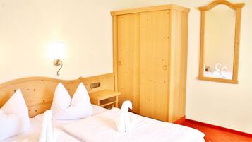 Une chambre d’hôtel avec un lit en bois, des oreillers blancs, une armoire en bois, une table de chevet et un miroir fixé au mur.
