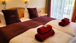 Habitación de hotel con dos camas, cada una con sábanas blancas y una manta roja. Dos lámparas de pared a cada lado de las camas, y una ventana con cortinas.