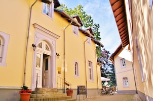 A yellow building with a white door and windows, a staircase, and a signboard.