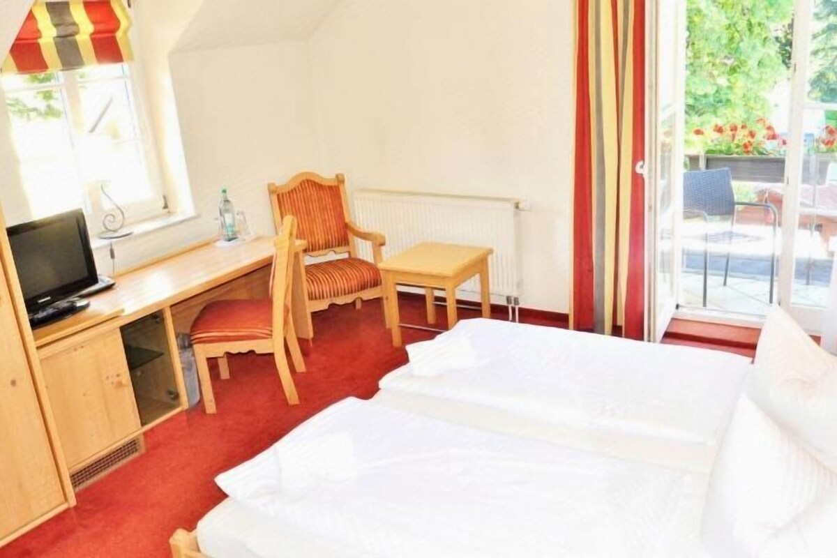 Una habitación de hotel con cama, escritorio con silla, televisión y ventana con cortinas.