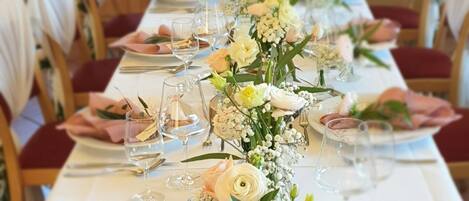 Een lange eettafel gedekt met witte tafelkleden, roze servetten en bloemstukken.