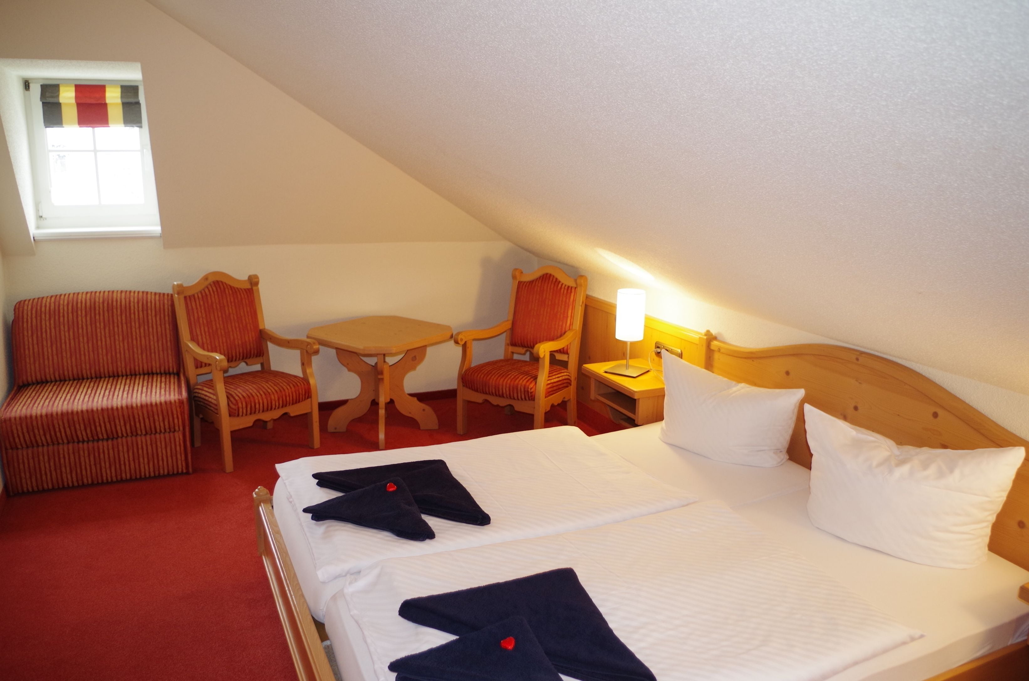 Ein Hotelzimmer mit zwei Betten, einer Sitzecke mit Stühlen und einem Tisch sowie einem Fenster mit gestreifter Vorhang.