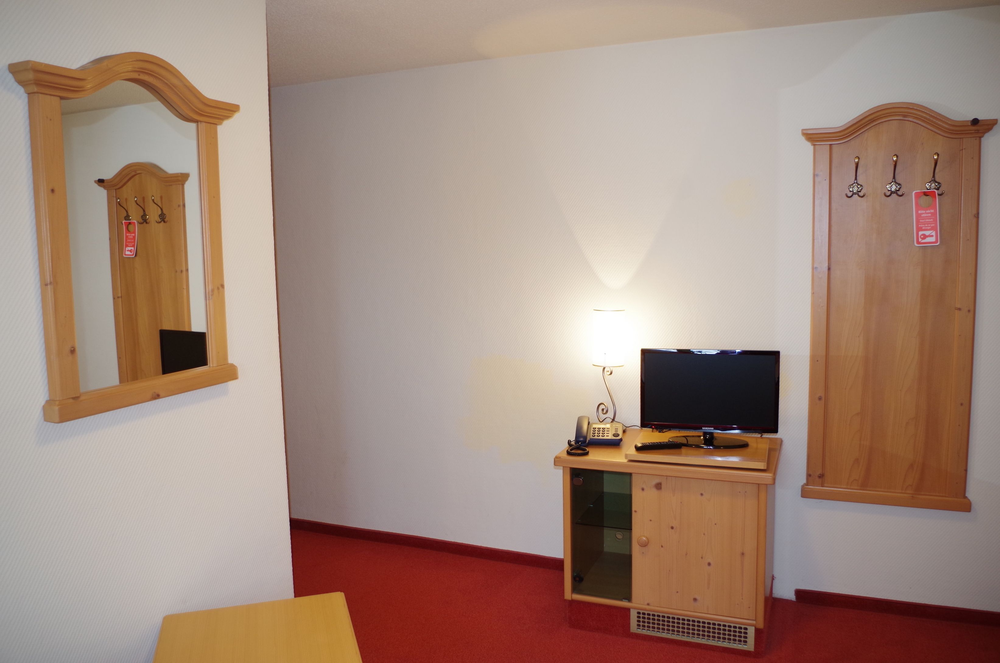 A room with a wooden cabinet, a flat-screen TV, a telephone, and a mirror with a wooden frame.