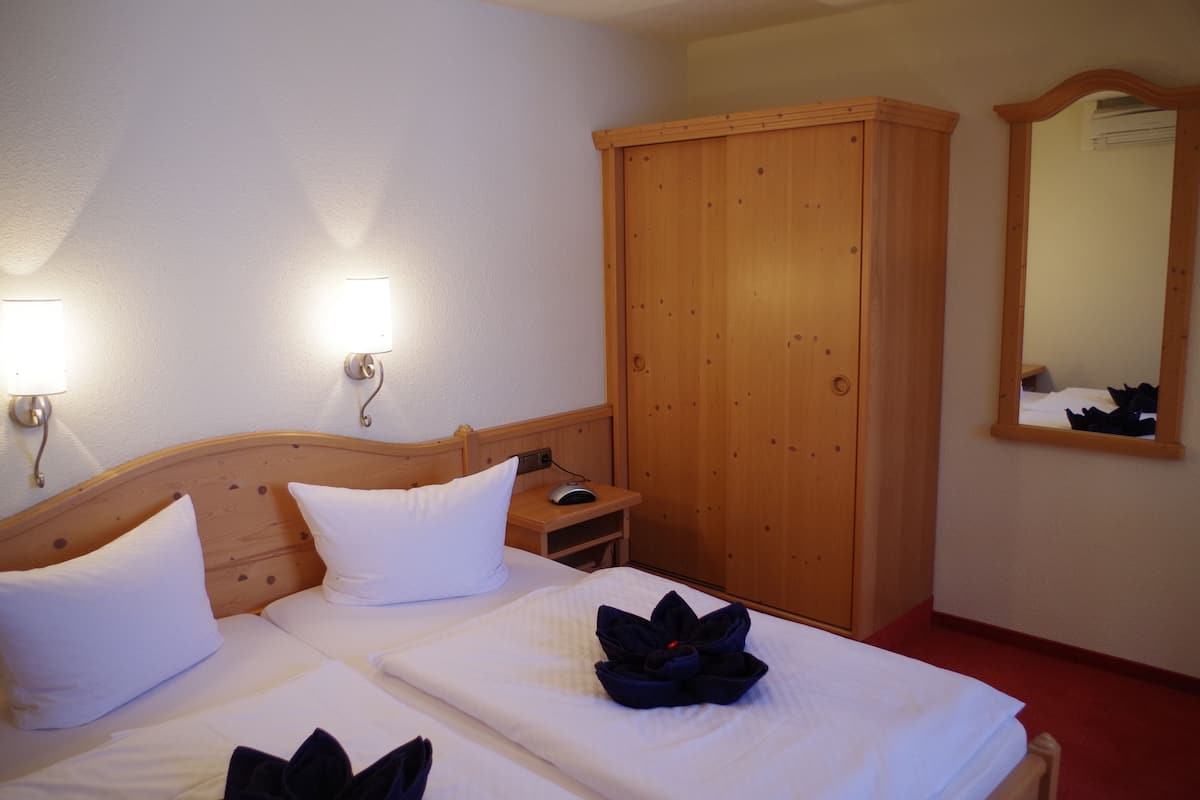 Habitación de hotel con una cama de madera, ropa de cama blanca, un armario de madera y un espejo en la pared.
