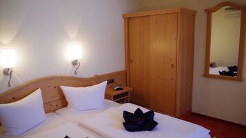 Une chambre d’hôtel avec un lit en bois, du linge de lit blanc, une armoire en bois et un miroir au mur.