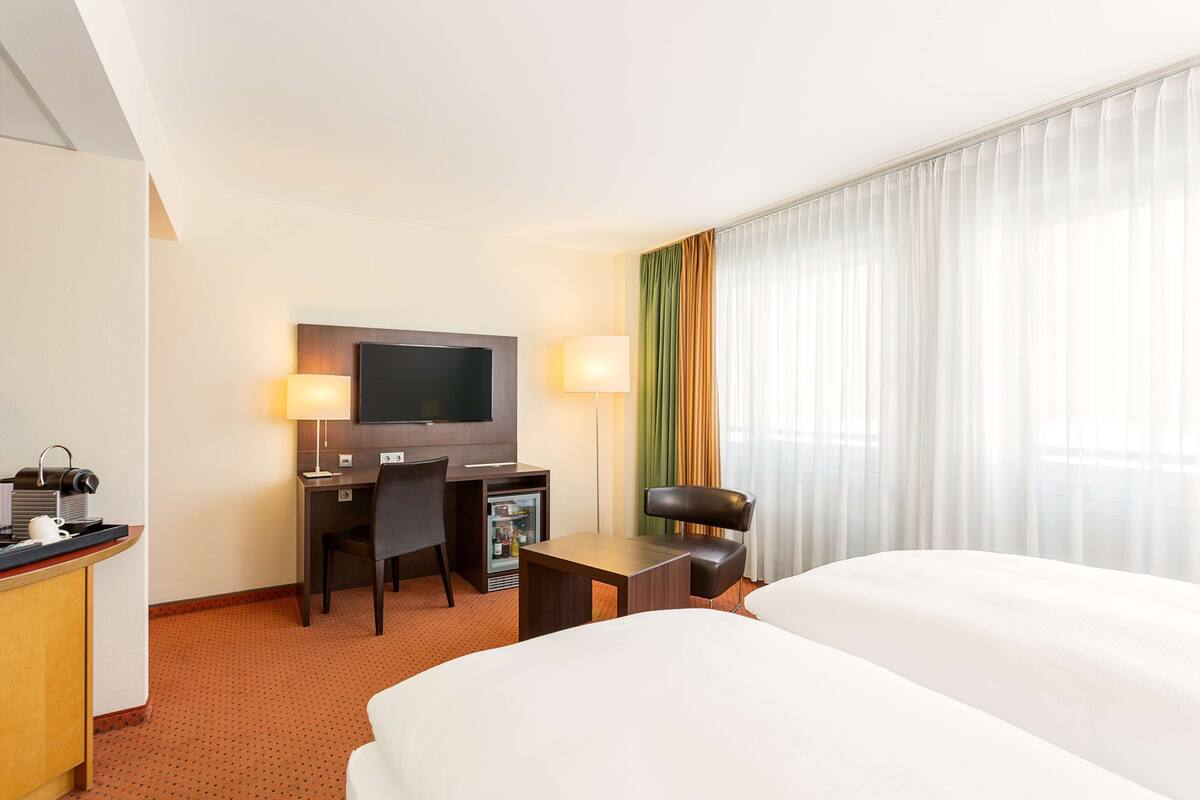 Une chambre d’hôtel équipée d’un lit, d’un bureau, d’une chaise, d’une télévision et d’un mini-bar.