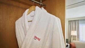 Una bata blanca con el logotipo de 'iStay Hotels' colgada de una percha de madera.