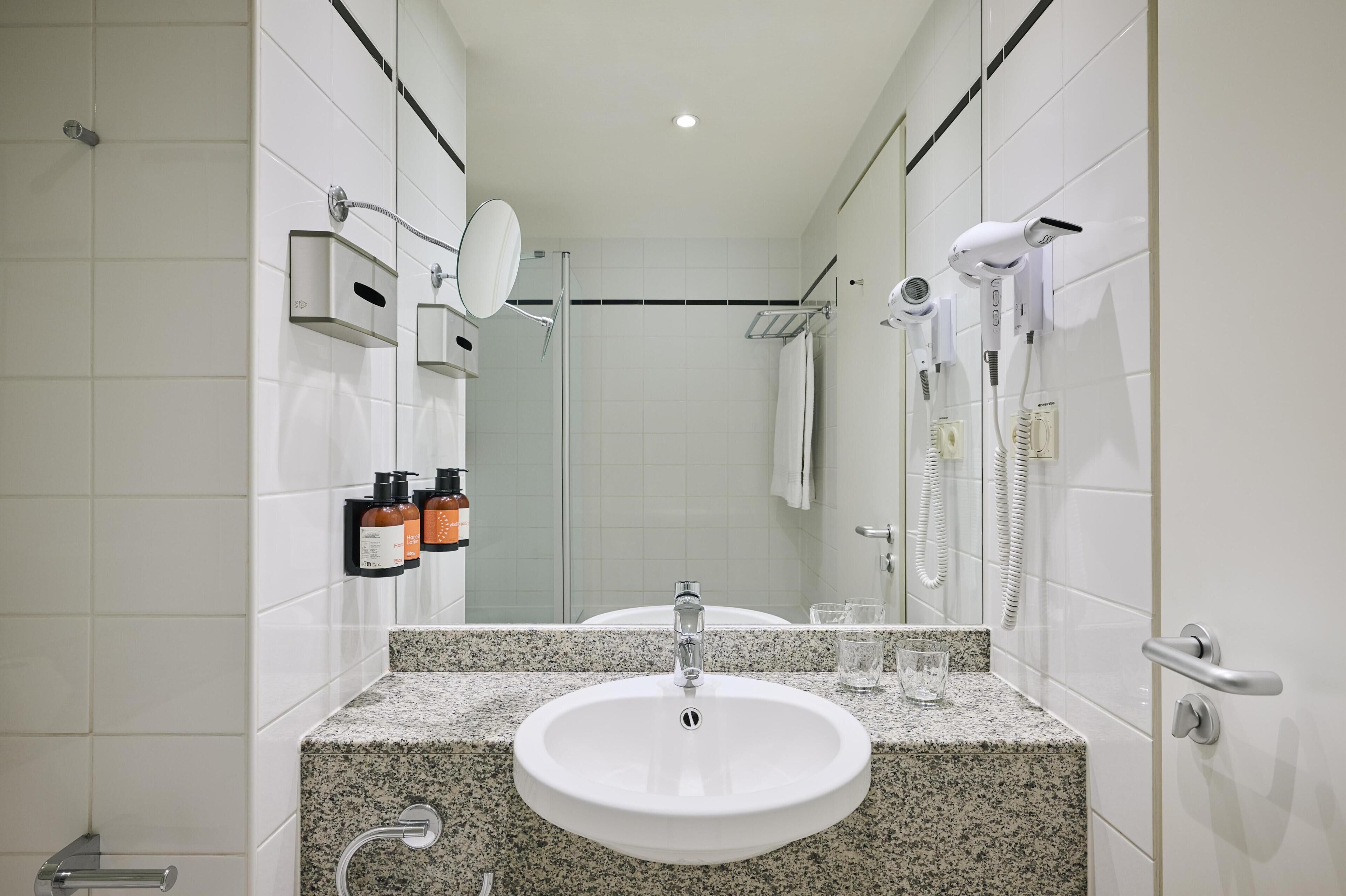 Ein modernes Badezimmer mit einer Granitplatte, einem weißen Waschbecken, einer Duschbrause, einem Haartrockner und einem Handtuchhalter.