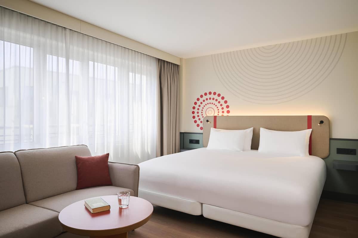 Une chambre d’hôtel avec un lit, un canapé, une petite table et une fenêtre avec des rideaux.