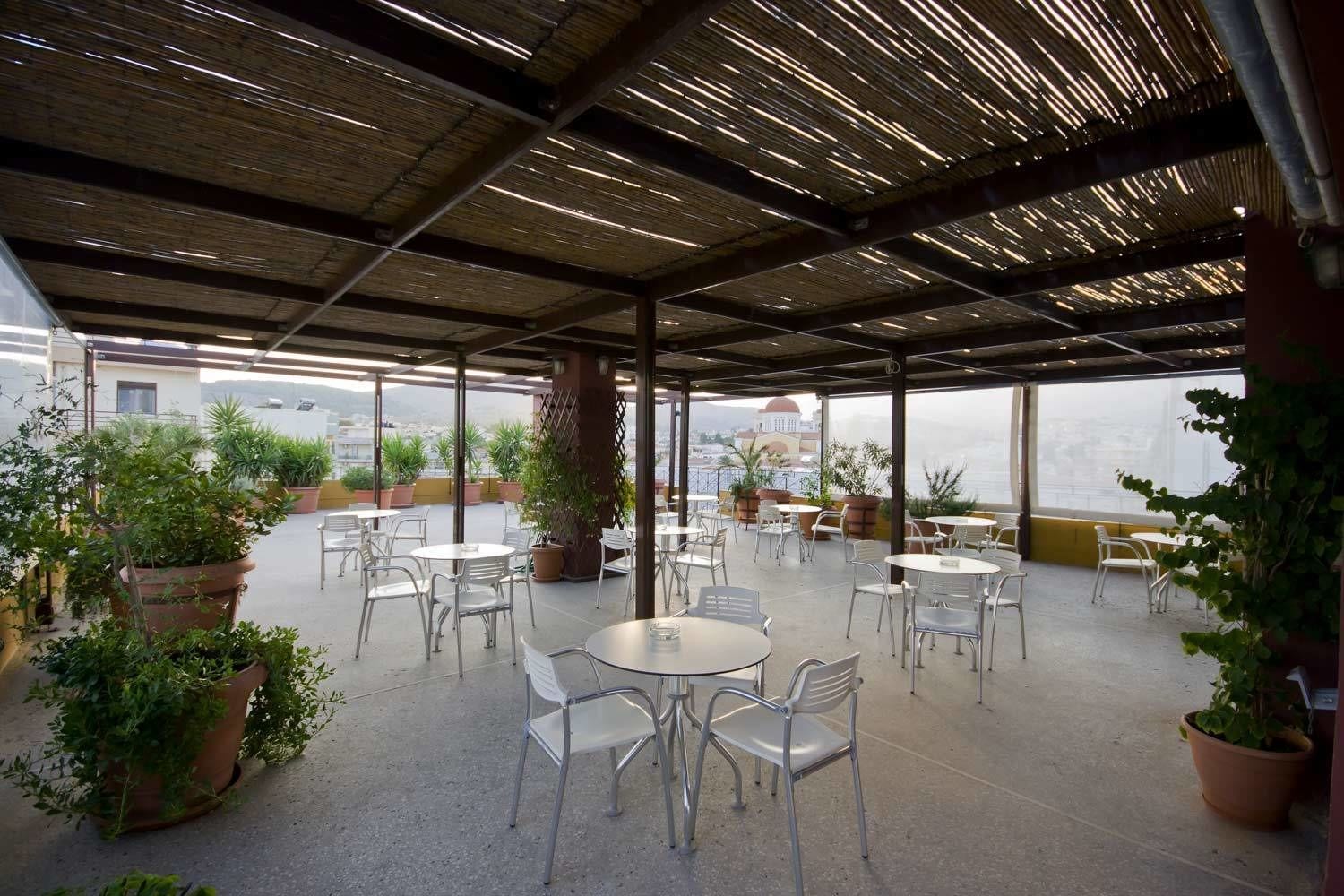 An outdoor patio with round tables and chairs, surrounded by potted plants.