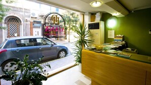 A reception area with a car parked outside, a reception desk, a potted plant, and a window with a view of the street. - Diana Hotel (Chios)