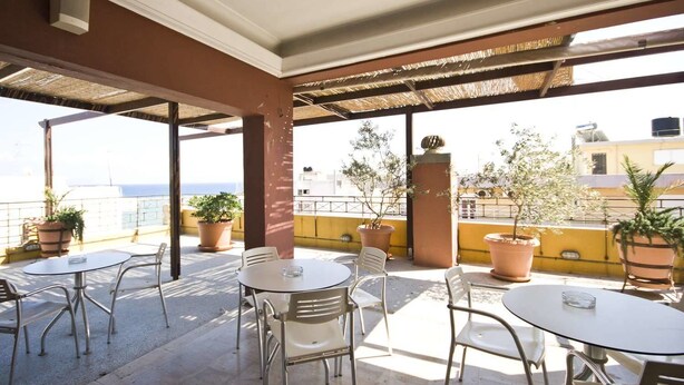 An outdoor patio area with round tables and chairs, potted plants, and a view of the sea. - Diana Hotel (Chios)