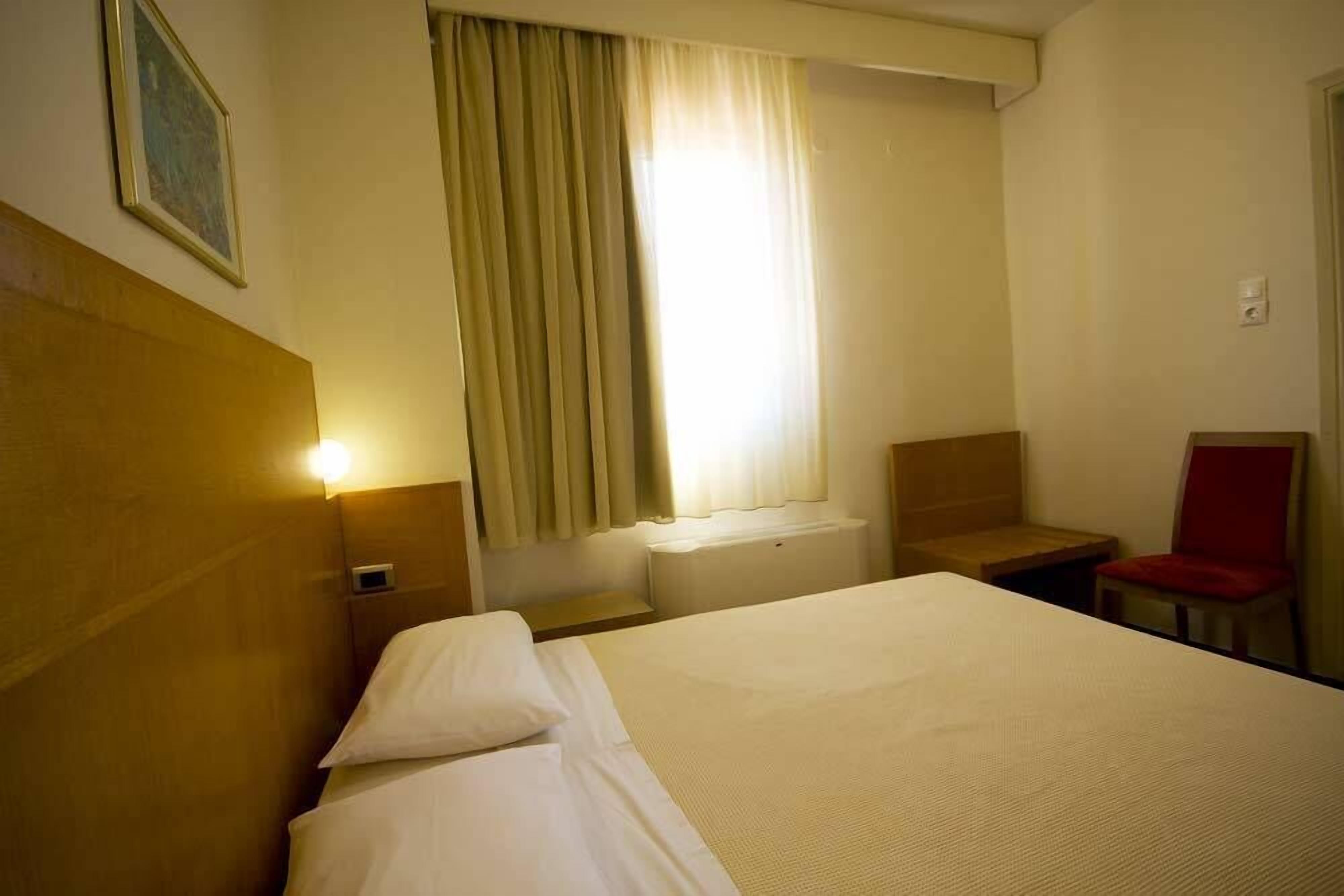 Una habitación de hotel con cama, una silla, una mesita y una ventana con cortinas.