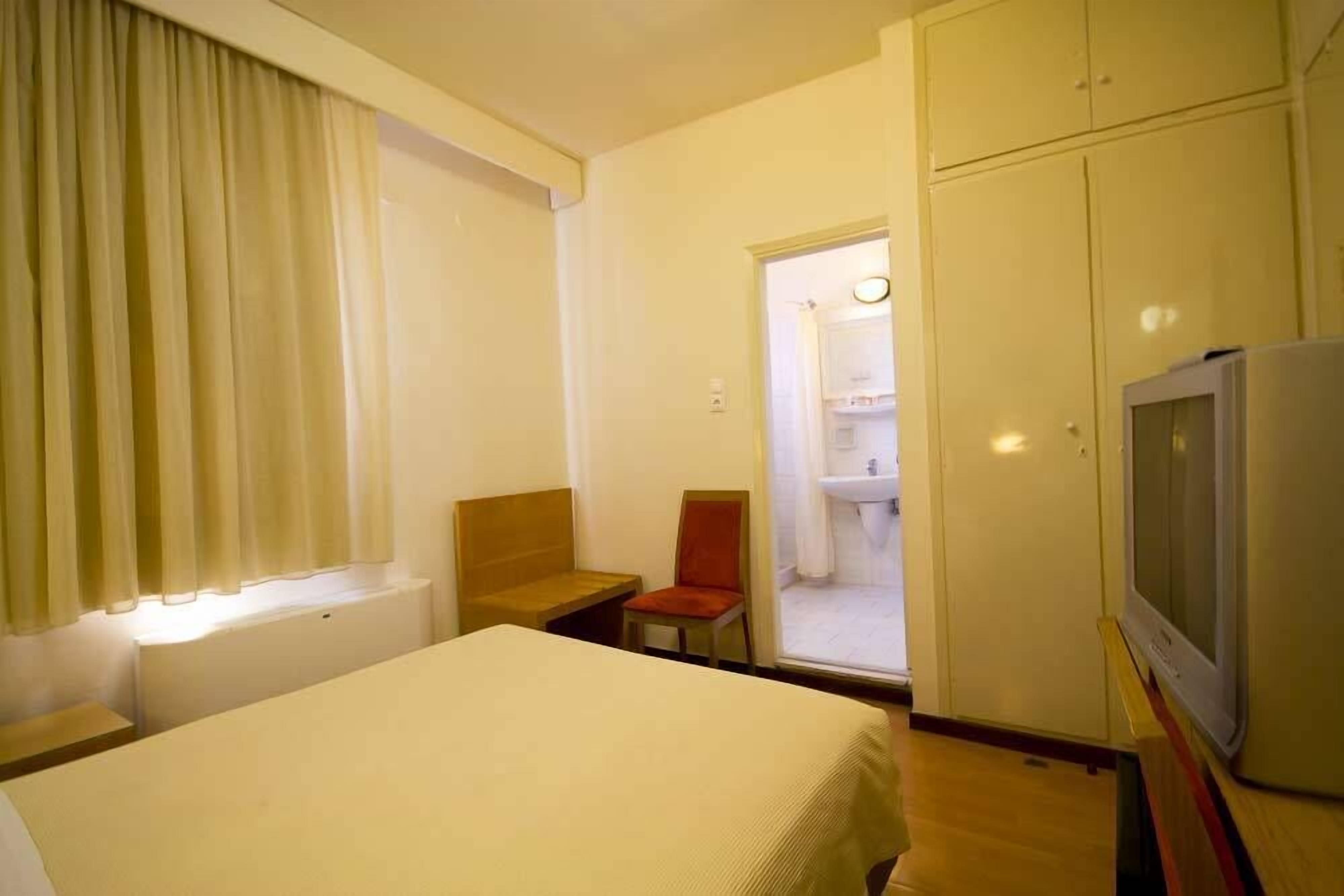 A hotel room with a bed, a chair, a television, and a bathroom visible through an open door.