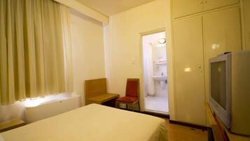 A hotel room with a bed, a chair, a television, and a bathroom visible through an open door.