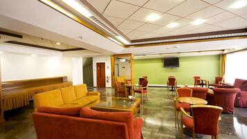 A hotel lobby with a seating area, a reception desk, and a television screen on the wall.