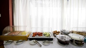 A buffet setup with various food items in clear containers, utensils on plates, and a window with sheer curtains in the background. - Diana Hotel (Chios)