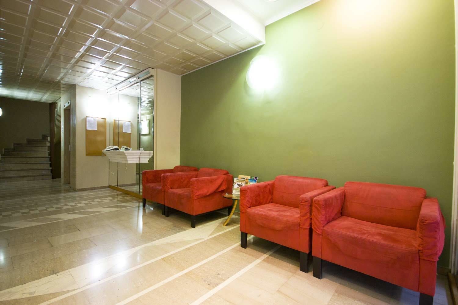 A reception area with a check-in counter, two red sofas, and a staircase in the background.