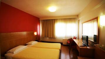 A hotel room with two beds, a desk with a TV, a chair, and a large mirror.