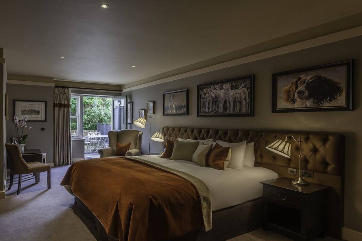 Un'ampia camera da letto con un letto grande, una zona salotto con una sedia e un tavolo, e opere d'arte alle pareti.