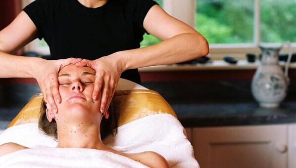 A person receiving a head massage in a room with a window and a vase on the counter.