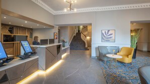 Zona de recepción de un hotel con mostrador, escalera y área de descanso.